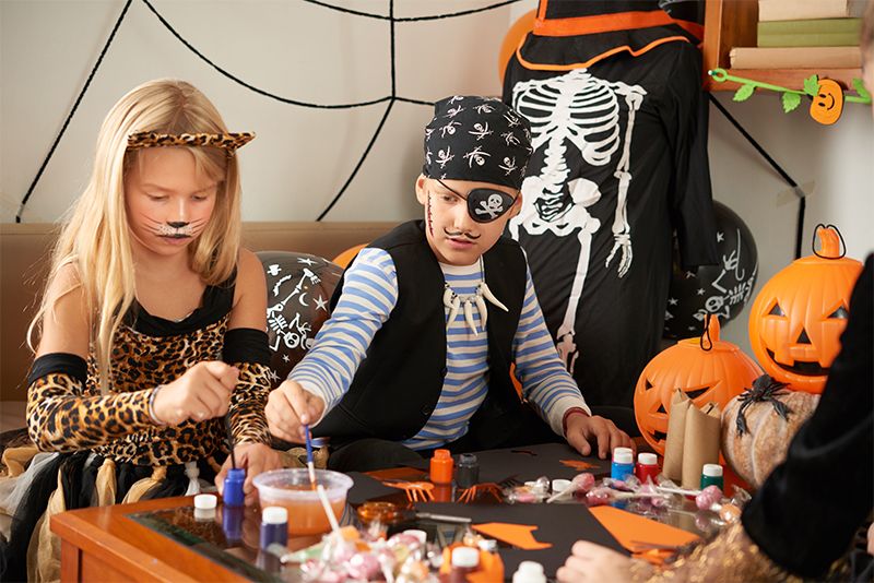 Young boy and girl dressed up in home made halloween costumes making halloween crafts from paper and card