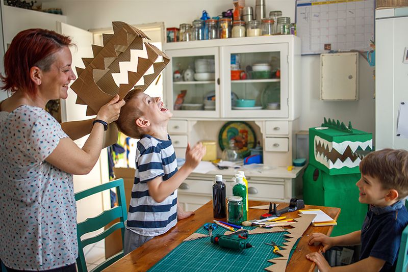 Mum helping son try on his home made cardboard dinosaur costume