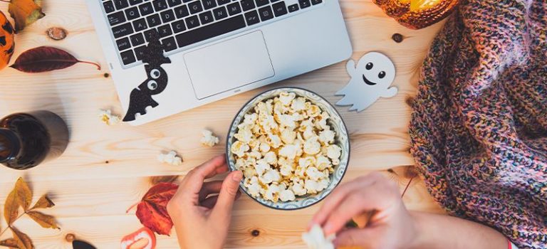 A bowl of popcorn and a laptop with DIY halloween decorations for a Halloween movie night